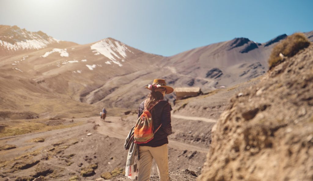 traveler hipster girl in hat with backpack exploring misty sunny rainbow mountain in Peru, South America
