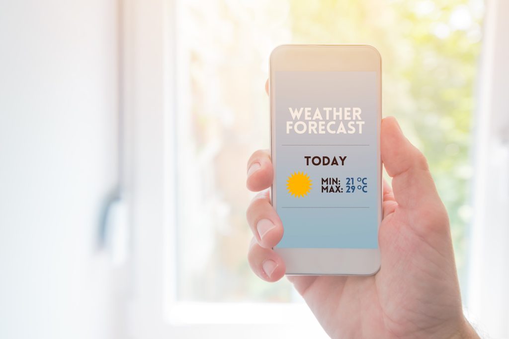 Weather forecast smartphone app mock up, man holding mobile phone with realistic simulated page of an application for meteorology and weather conditions prediction.